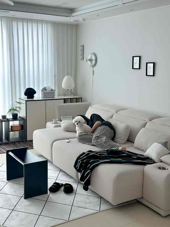 ベージュとホワイトのトーンのリビング、ソファと壁の照明が配されたモダンな雰囲気のインテリア