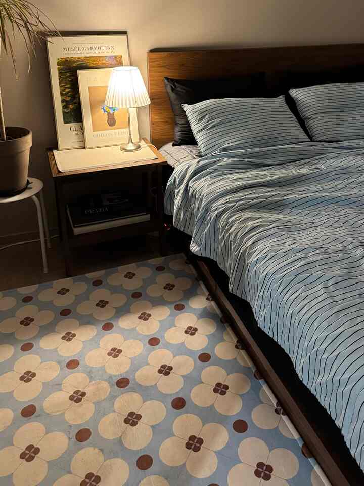 温かみのあるブラウンとブルーのトーンの寝室、木製ベッドと花柄ラグ、ナイトテーブルの照明が印象的な空間