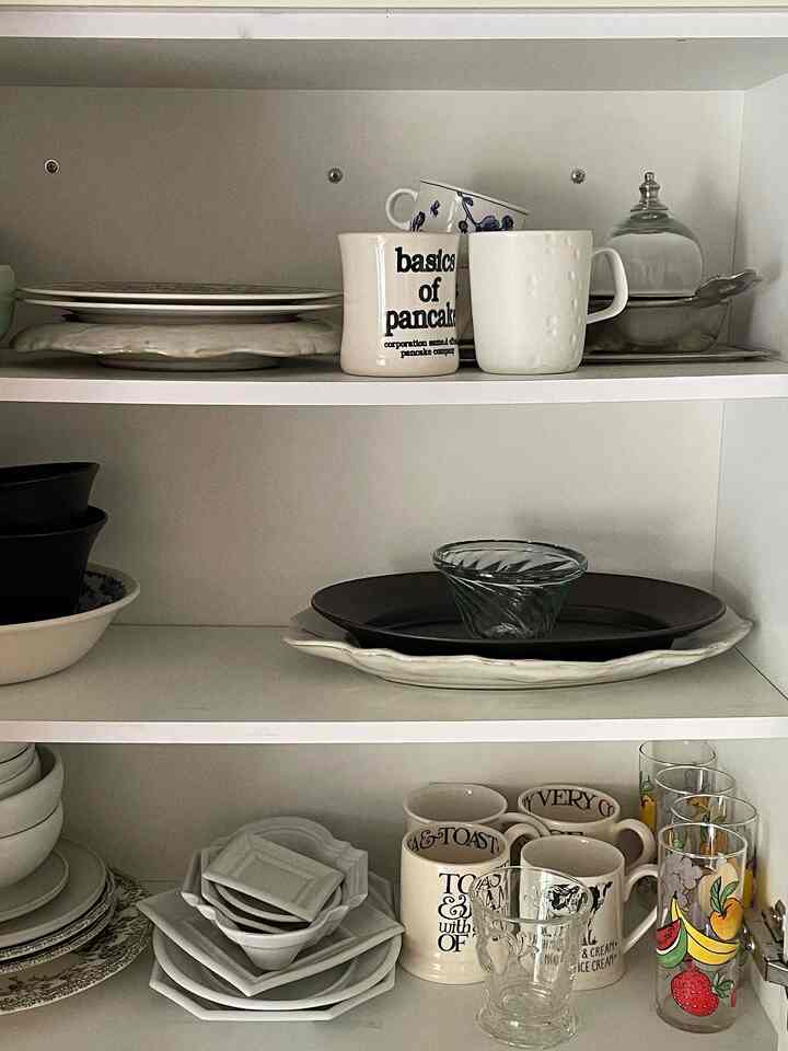 白を基調としたキッチンキャビネット、整然と並べられた様々な食器とマグカップ、グラスが見えるシンプルなインテリア
