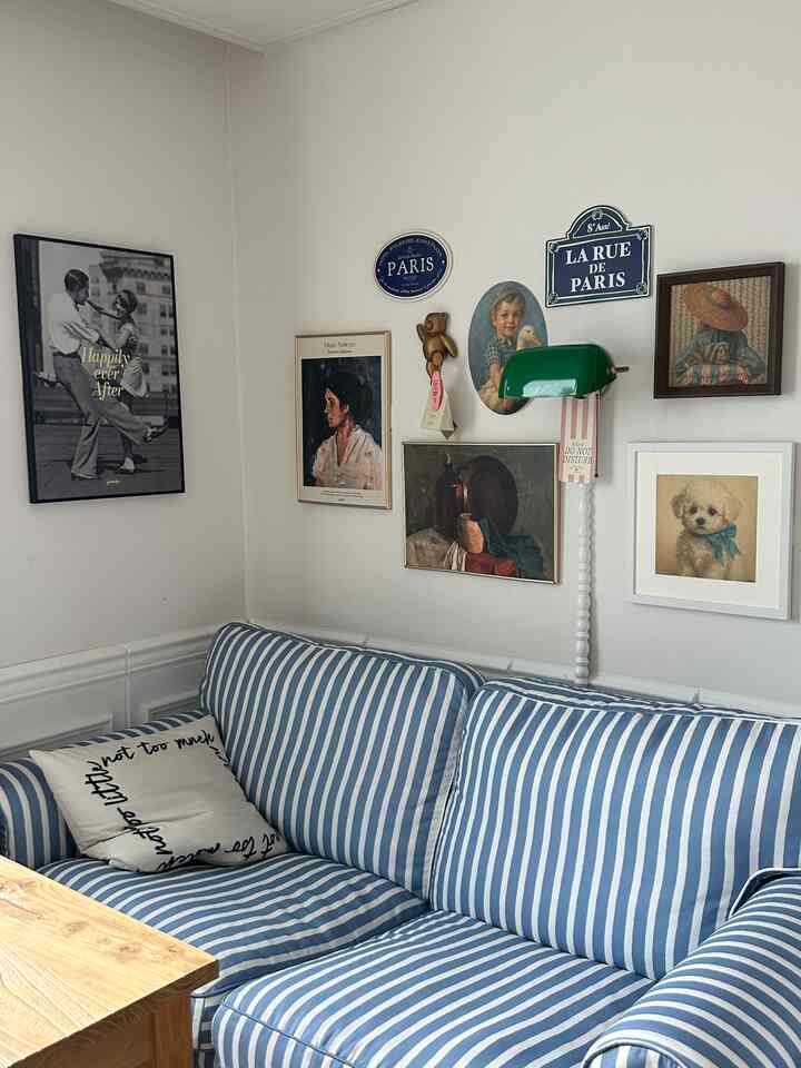 ブルーとホワイトのストライプ柄ソファが配置されたビンテージ風フレンチカントリーのリビング、壁には様々なヴィンテージの額縁やポスターが飾られている印象的な空間