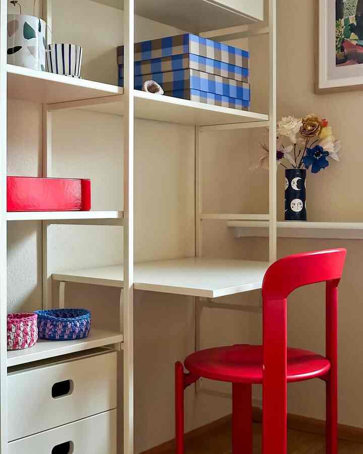 White desk and shelves arranged in corner space with a vivid red chair, creating a cozy home office setup