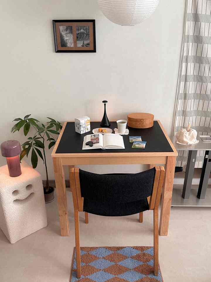 ナチュラルウッド調のホームオフィス空間、木製の机と黒い椅子、ラグと植物が配置された雰囲気のある部屋