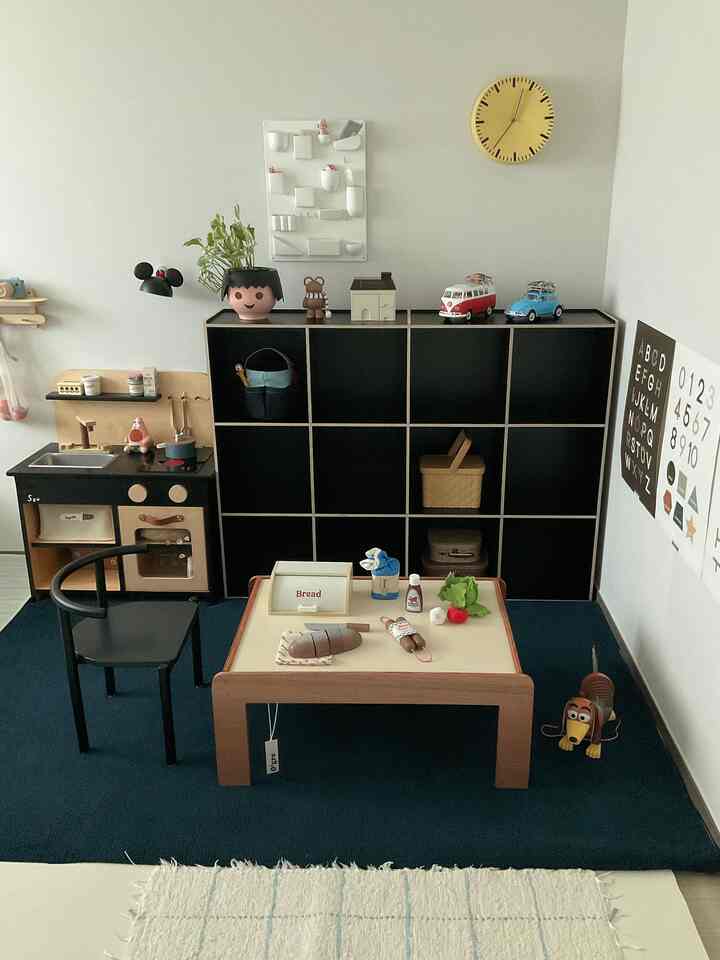 明るい色調の子供部屋、木製テーブルと黒い本棚が配置されたシンプルで整った遊びスペース