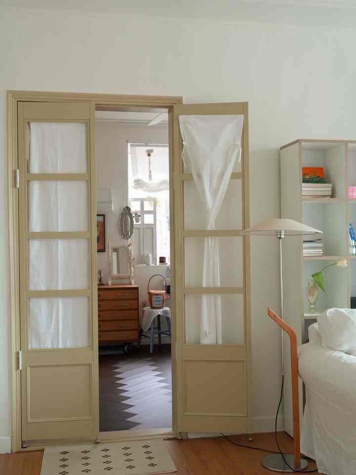 ナチュラルな色調のリビング、ベージュのドアと白いソファ、フロアランプが配置された落ち着いた雰囲気のインテリア