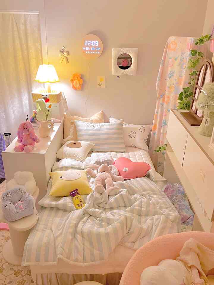 柔らかなパステルカラーと多彩なクッション、かわいらしいぬいぐるみが配置された、暖かみのある寝室空間