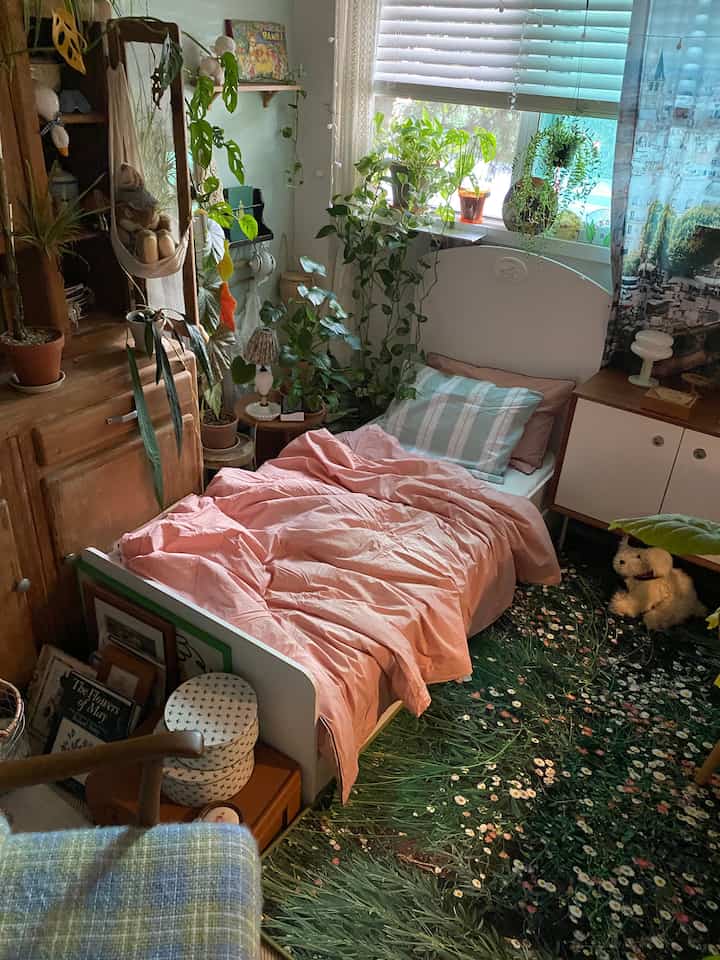 ピンクの寝具とホワイト家具が配置された、植物と木目調の家具が調和するヴィンテージで自然な印象の寝室