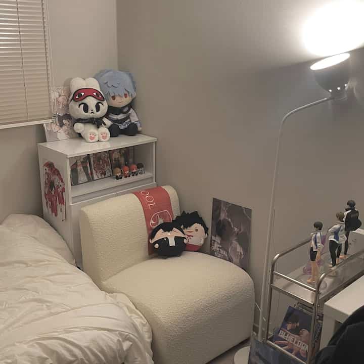白を基調としたミッドセンチュリーモダンの狭いワンルーム、アニメのフィギュアとぬいぐるみが配置された雰囲気のあるオタクルーム