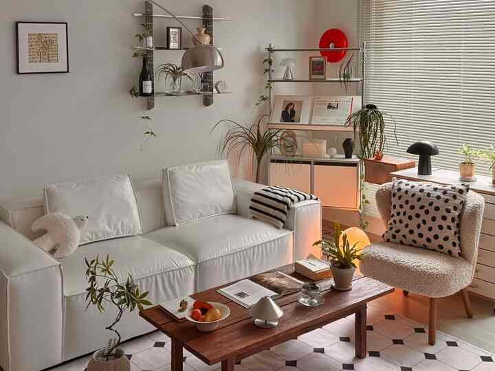 ホワイトとブラウンのトーンでまとめられたモダンなリビング、ソファとアームチェア、木製テーブルと棚、照明が配置された雰囲気のある空間