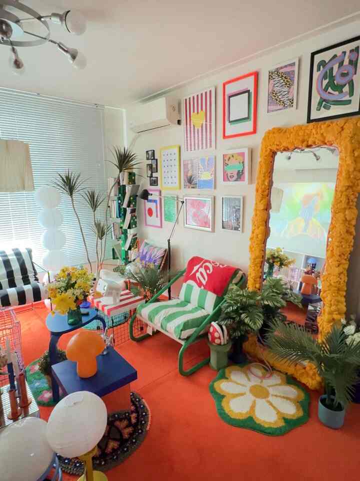 Cozy natural-toned living room with a bright orange rug, colorful wall art, large yellow textured mirror, and green armchair