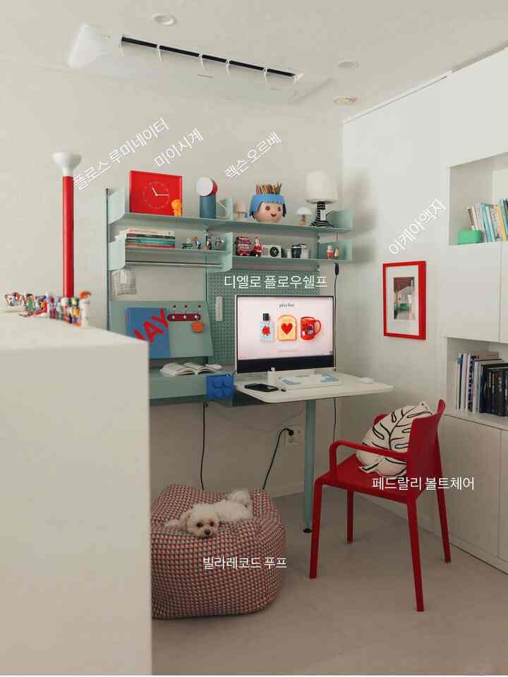 白い壁と床、赤いアームチェアとディエロのフロウシェルフデスクが置かれたコンパクトなホームオフィス、犬がいる落ち着いた雰囲気のインテリア