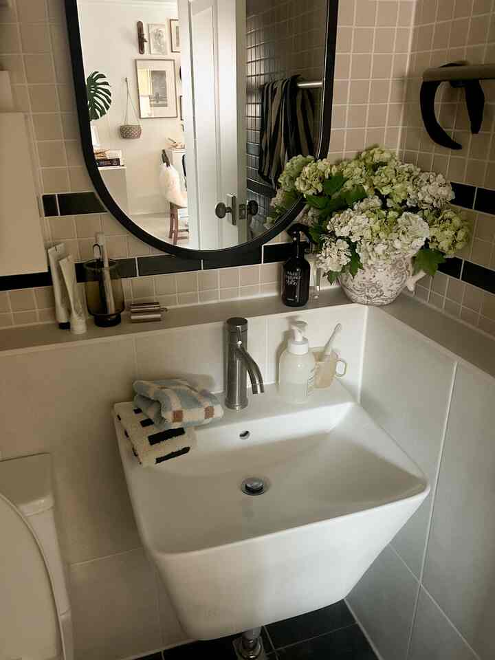Modern bathroom with white and gray tiles, featuring a sink, towels, and a plant pot arranged neatly