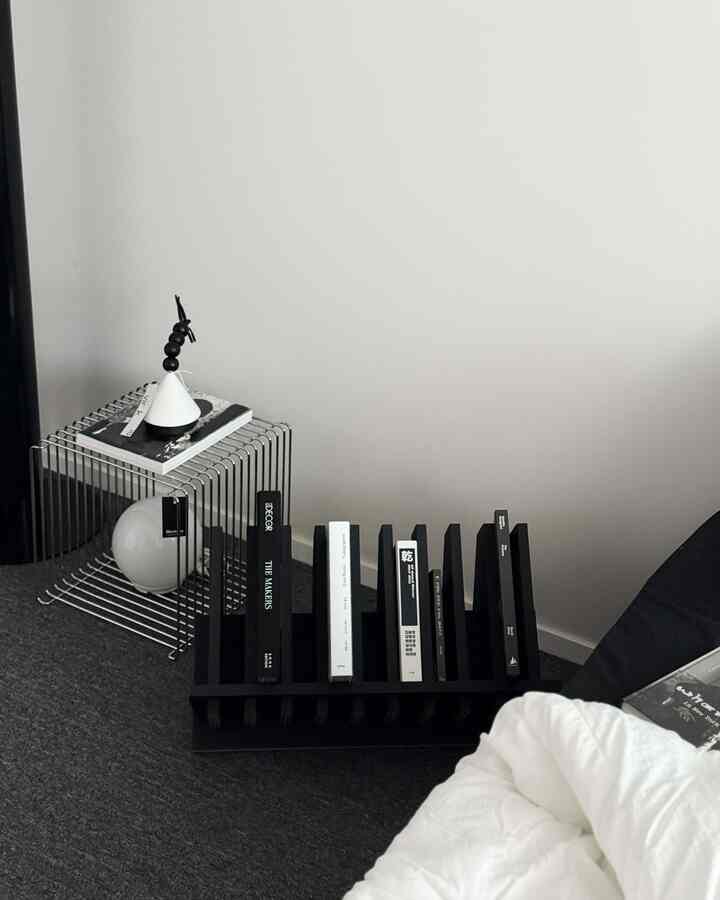 Minimal bedroom with white walls, black bookshelf, and metal nightstand featuring monochrome decor