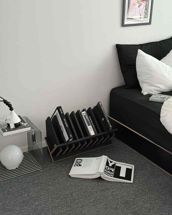 Monotone living room with black sofa, magazine rack, and gray carpet in a minimalistic setting