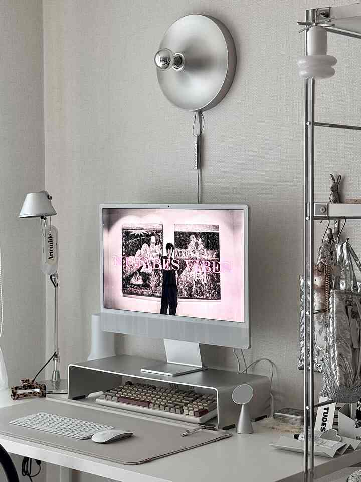 Compact home office in silver and white tones, featuring a monitor stand and wall sconce in a simple modern workspace