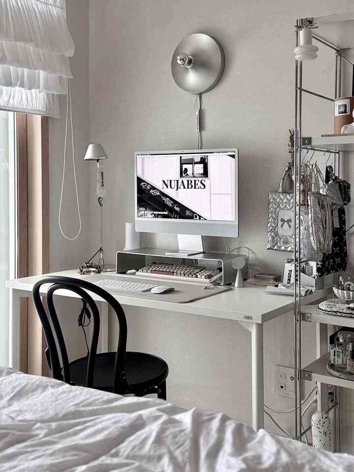 Minimal white and silver toned small home office featuring a neat desk with computer in a clean and modern style