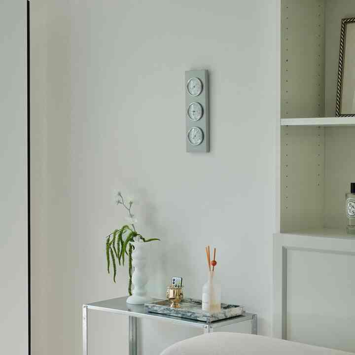 Minimal interior space with white and silver tones featuring a metal shelf, diffuser, and vase in front of a wall