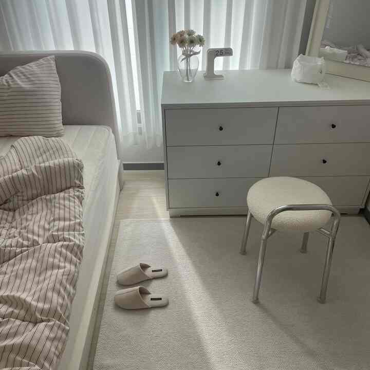 White-toned bedroom featuring a beige striped duvet cover and storage dresser in a simple, clean space
