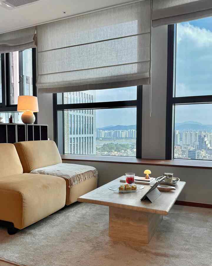 ベージュのトーンが特徴のワンルームリビング、大きな窓とベージュのソファ、石のコーヒーテーブルが配置された落ち着いたインテリア