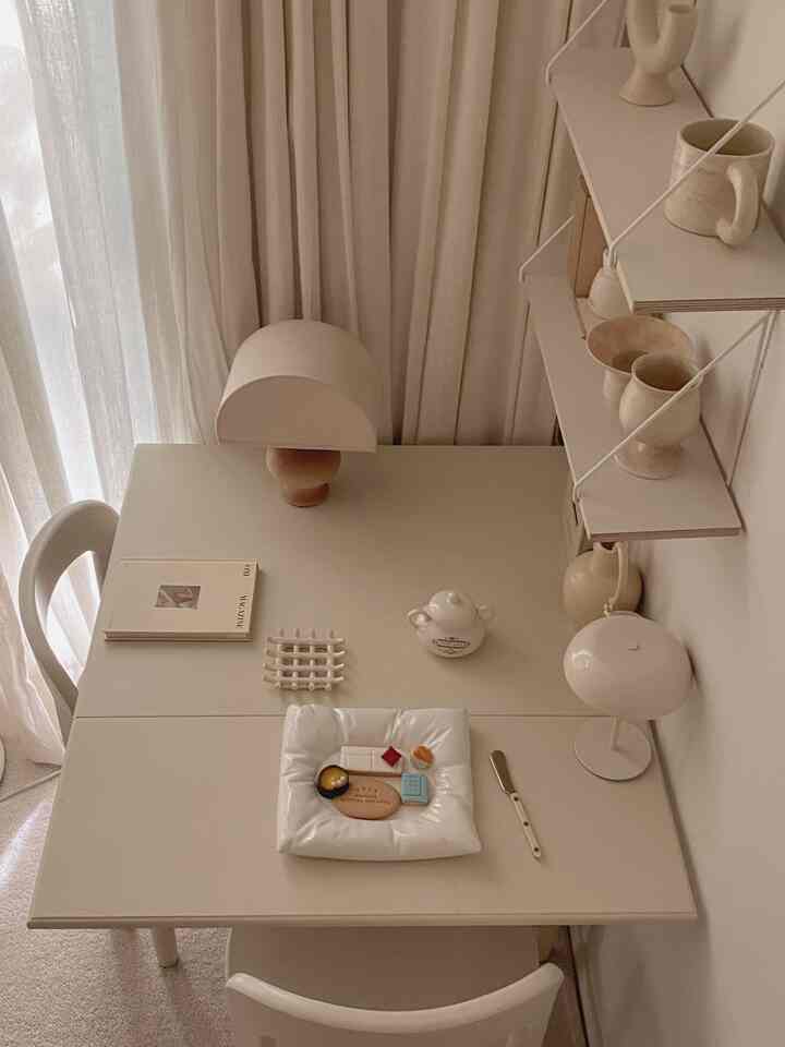 ベージュトーンのダイニングルーム、シンプルな家具とカーテン、テーブルランプとオブジェが配置された雰囲気のある空間