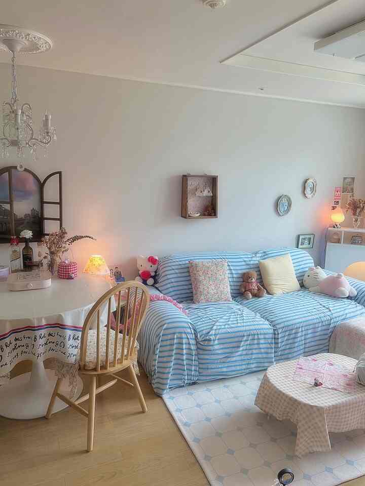 スカイブルーとライトブラウンの色調のリビング、ストライプのソファと木製チェア、壁掛け飾りとかわいらしいクッションが配置されたヴィンテージ感のある暖かなインテリア