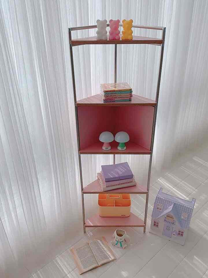 明るいピンクのコーナーシェルフが白い床とカーテンと調和した空間に、クマのオブジェとミニムードランプが配置された清潔感のあるインテリア