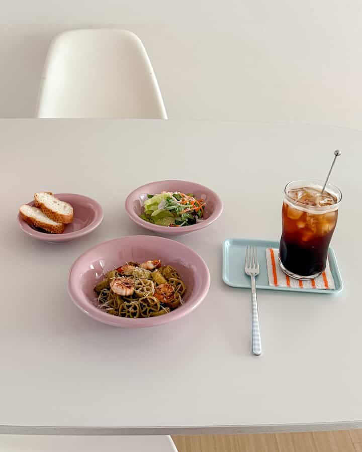 白と淡いピンクのトーンのダイニング空間、ミニマルで整えられた食器とコーヒーが置かれた清潔なテーブル