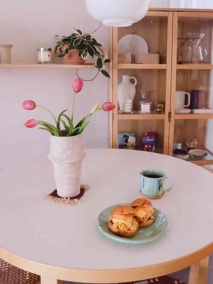 白と木目調の調和が美しいダイニング、中央の丸テーブルに花瓶とコーヒーカップが置かれた雰囲気のあるインテリア