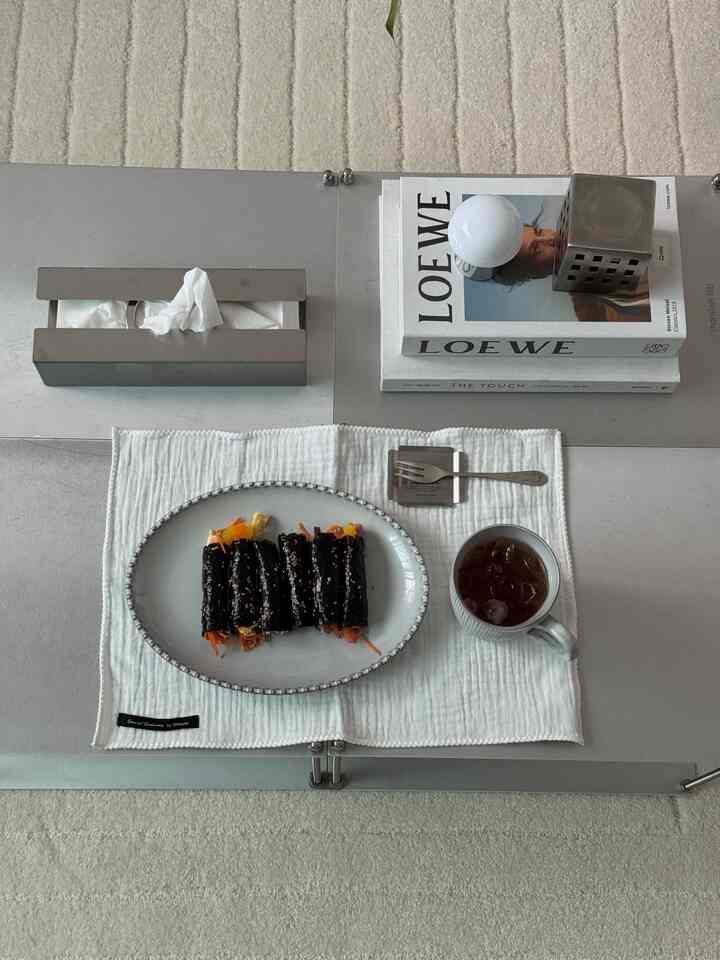 White-toned modern dining table featuring a minimal table runner, plate of kimbap, and iced drink in a clean setting