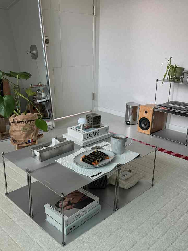 Modern living room in white and silver tones featuring a metal coffee table, large mirror, and green plant creating a balanced atmosphere