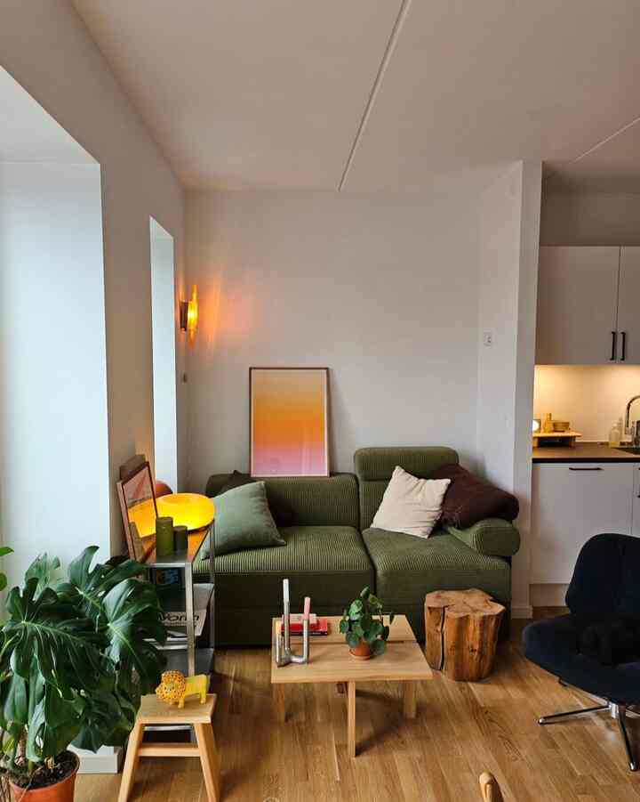 Green and wood tone living room featuring sofa, plants, and warm lighting creating a cozy atmosphere