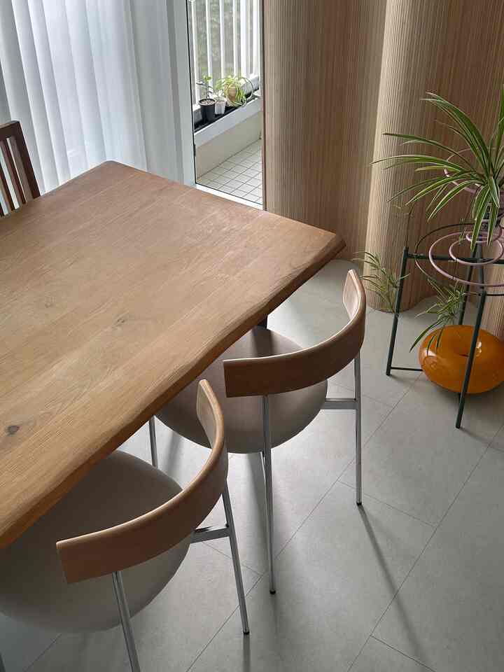 ナチュラルな木目調とベージュの色合いが特徴のダイニング、木製テーブルと椅子、植物が配置されたモダンで落ち着いた空間