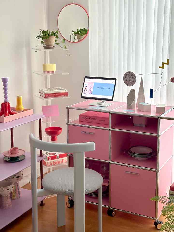 ピンクと白の色調のホームオフィス、モジュラー収納とアクリル棚が配置された雰囲気のある作業空間