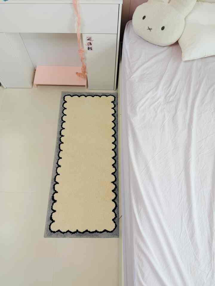 明るいホワイトとベージュ調の子供部屋、赤ちゃん用クッションのあるベッドとシンプルなラグが配置された清潔感のある寝室