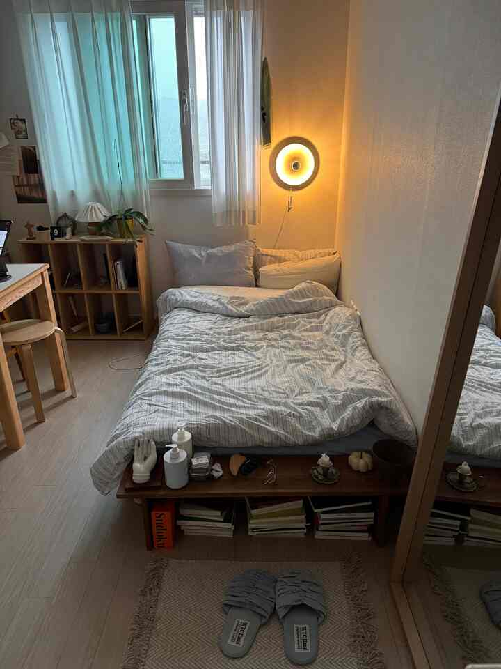 白とベージュの色調の寝室、ベッドとカーテン、壁の照明が配置された雰囲気のある北欧スタイルの空間