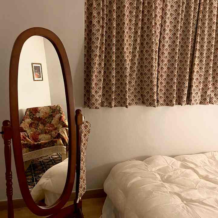 ブラウンの木目調とヴィンテージ柄のカーテン、花柄のヴィンテージチェアが鏡に映る寝室の雰囲気のあるインテリア
