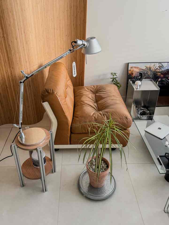 ブラウンの木目調の壁とレザーソファがあるモダンなリビング、シルバーの照明、ガラスのテーブル、鉢植えが配置された温かみのある空間