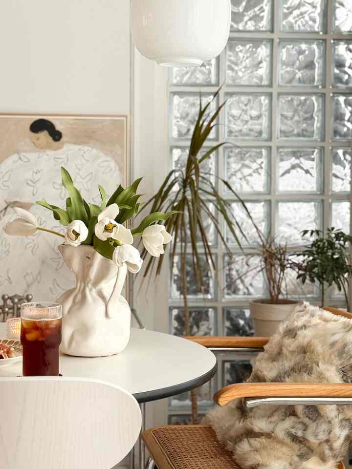 White and wood-tone living dining space featuring a vase with flowers and plants creating a natural modern atmosphere