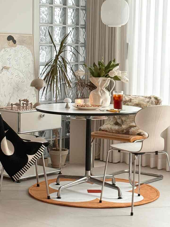 Bright white and light brown toned dining room featuring a round dining table, plants, and curtains creating a modern ambiance
