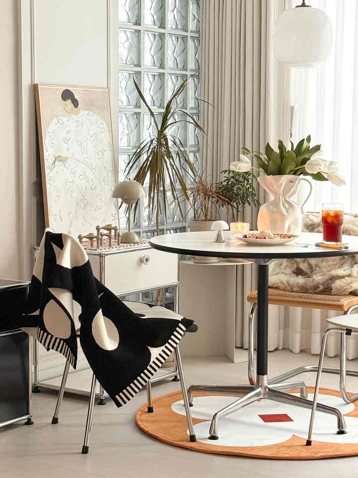 Modern dining room in white and black tones featuring a round dining table and plants creating a refined atmosphere