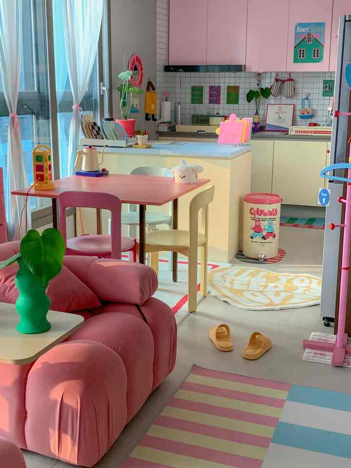 A pink-toned living room and kitchen featuring a soft sofa and colorful dining chairs in a bright, cozy space
