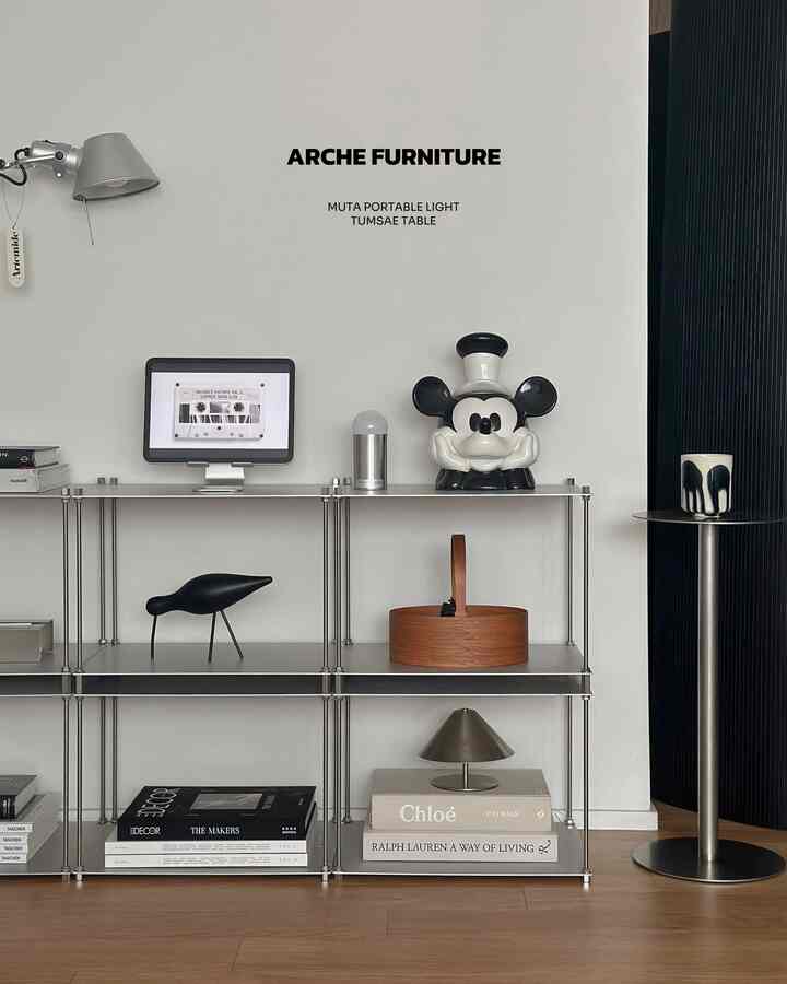 白い壁とシルバーの金属棚、ミニマルなオブジェが配置されたモダンでシンプルなリビングインテリア