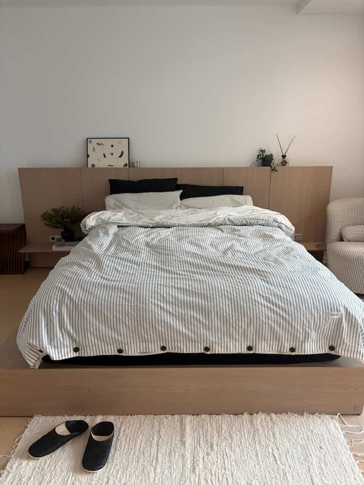 A white and wood-toned bedroom featuring striped bedding and black pillows, creating a simple and modern atmosphere