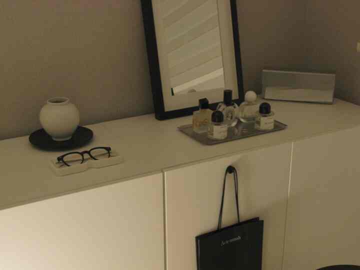Soft white and gray toned entrance space featuring a black-framed mirror, tray with glass bottles, and minimalist storage cabinet