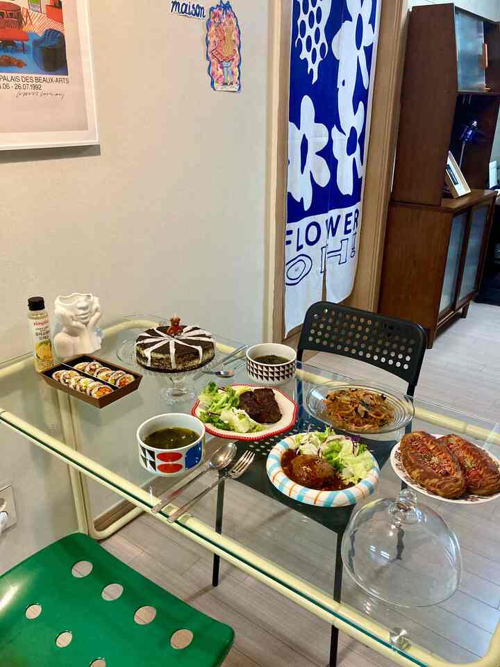 ナチュラルカラーのキッチンダイニング、透明なガラステーブルに誕生日ケーキや様々な料理が並ぶ雰囲気のあるホームパーティー空間