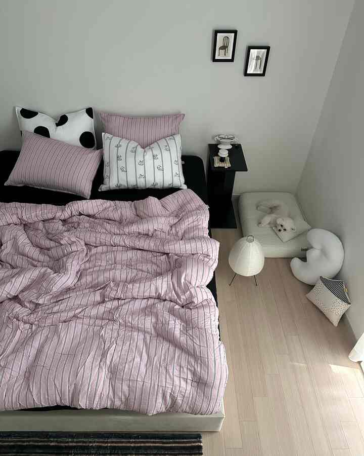 Cozy bedroom with pink striped bedding, white walls, and a small pet dog lying on a pet bed