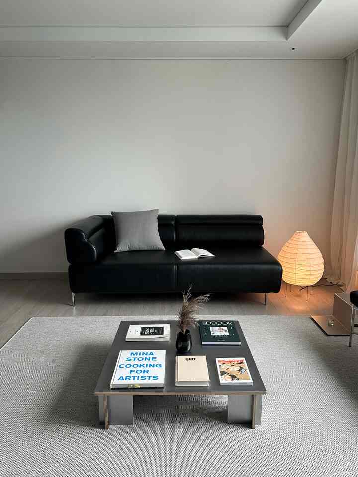 Modern toned living room featuring a black leather sofa, gray rug, and a coffee table arranged simply and elegantly in the center