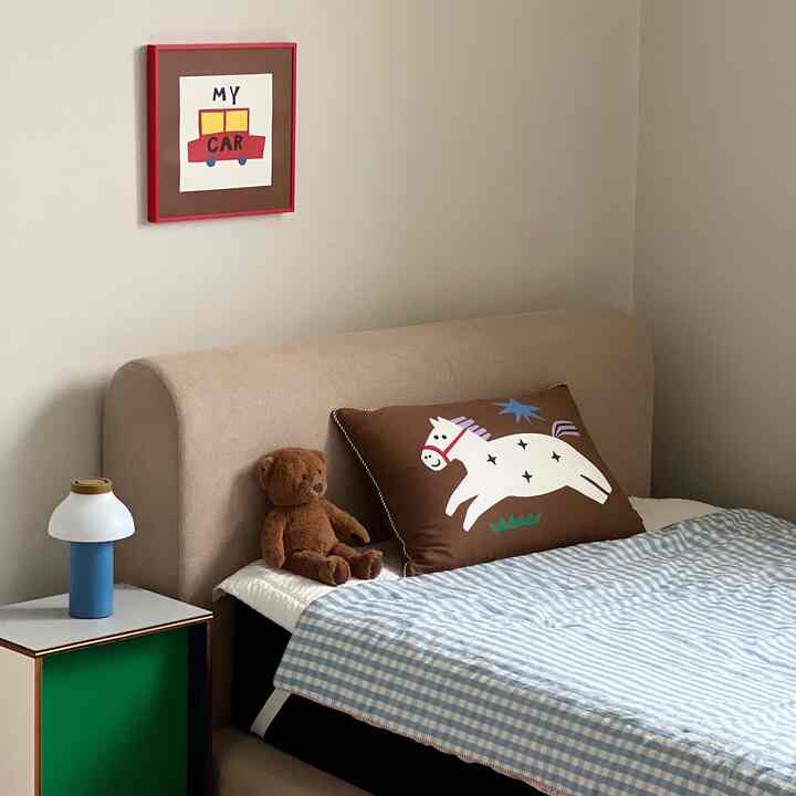 ベージュとブルーの色調の子供部屋、可愛い動物の枕とテディベア、テーブルランプが置かれた温かみのある寝室