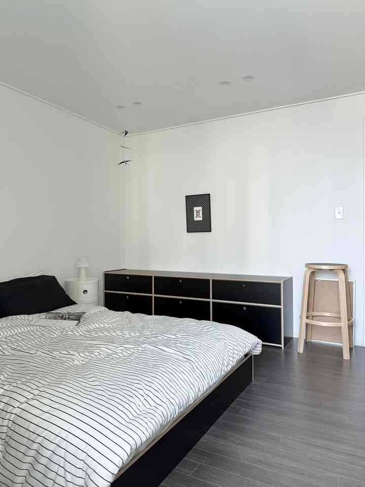 白と黒、グレーのトーンでまとめられたモダンな寝室、ストライプの寝具と黒のチェストが配置されたすっきりとした空間