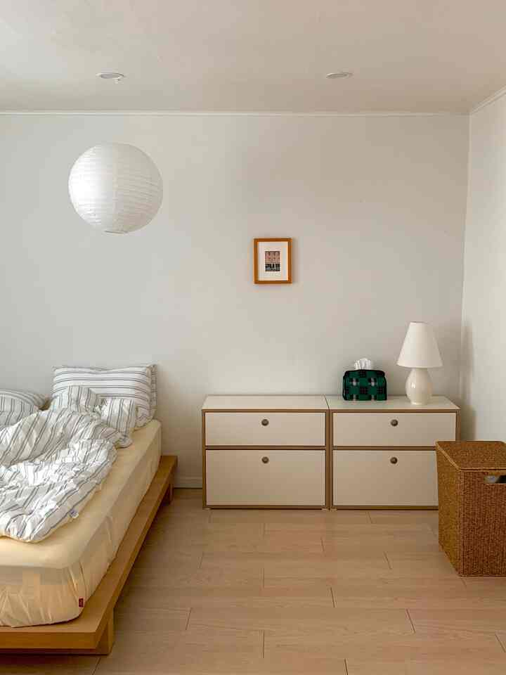 白と木目調の寝室、ミニマルな家具構成と整えられたベッドが配置された落ち着いた雰囲気の空間