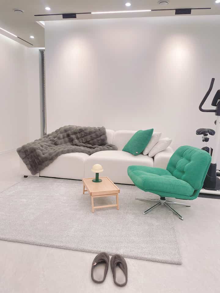 明るいホワイトとグリーンのトーンのリビング、白いソファと緑のアームチェア、グレーのラグが置かれた落ち着いた空間